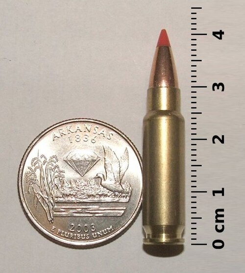Photo of a 5.7×28mm SS196SR cartridge next to a U.S. quarter-dollar coin and ruler, in a size comparison.