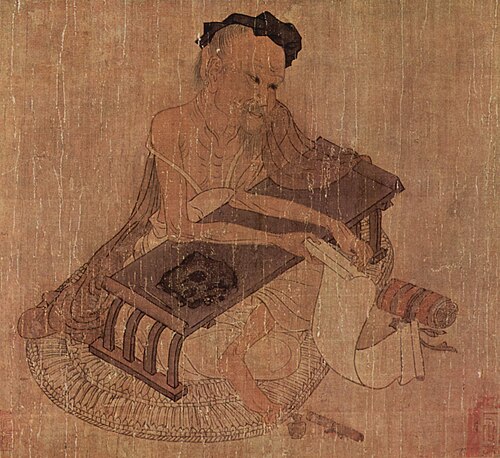 رجل صيني مسن يجلس على مكتب كتابة منخفض ويحمل لفافة