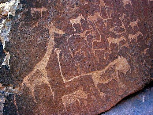 لوح من الحجر الرملي البني الداكن مُغطى بنقوش صخرية بنية فاتحة. تُظهر النقوش جميعها حيوانات أفريقية، مع زرافة ضخمة على اليسار. في المنتصف، يوجد مخلوق خيالي على هيئة أسد بأصابع قدم بشرية وذيل طويل بشكل غير معقول. في طرف الذيل، توجد علامة قدم بستة أصابع.