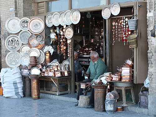 رجلان يصنعان مصنوعات يدوية معدنية أمام متجر