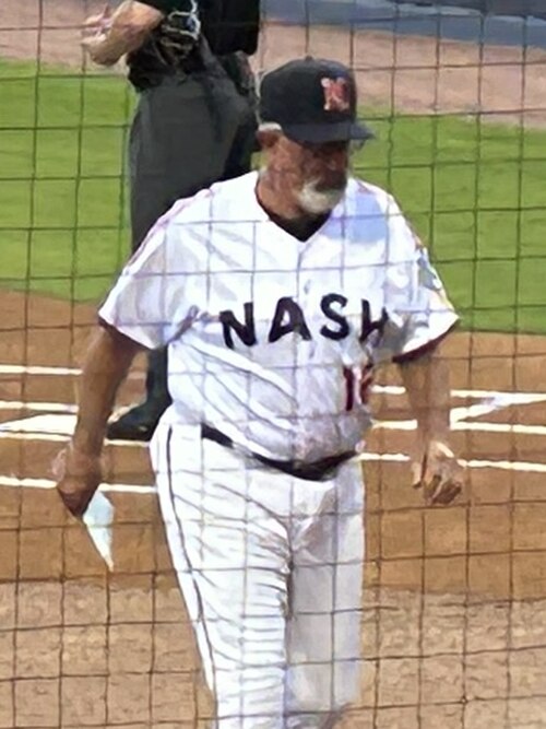 رجل يرتدي زي بيسبول أبيض اللون كُتب عليه "NASH" بأحرف زرقاء داكنة على صدره، ورقم "16" أحمر أسفله، وقبعة زرقاء داكنة عليها حرف "N" أحمر وأبيض في الأمام، يسير نحو مقاعد البدلاء.
