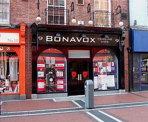 متجر يُدعى "Bonavox Hearing Aids"، يقع على طريق مرصوف بالطوب وبجوار متجرين آخرين.