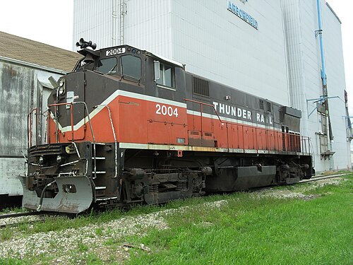 قاطرة ديزل متوقفة على سكة حديد أمام مبنى صناعي. تحمل الرقم 2004، ومكتوب على جانبها "THUNDER RAIL". طلاءها مميزٌ بلا شك لسكك حديد بروفيدنس ووستر، حيث يظهر اللون الأحمر الخاص بالسكك الحديدية في الجزء السفلي والبني في الجزء العلوي، ويفصل بينهما خط أبيض ينخفض ​​ثم يرتفع في مقدمة القاطرة.