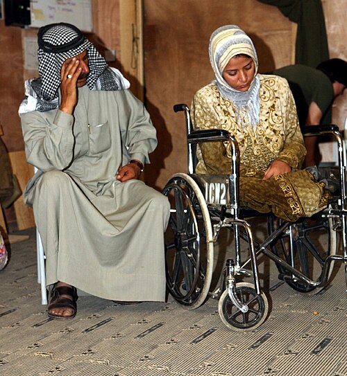 امرأة تجلس على كرسي متحرك مع وجود أفراد عسكريين في الخلفية