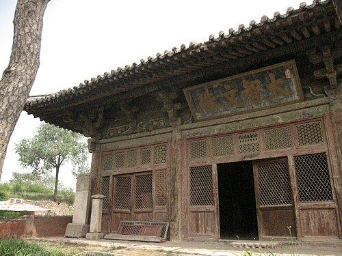 نصف مبنى ذي جدران حمراء وأفاريز كبيرة بارزة من الزاوية. يظهر جذع شجرة على الجانب الأيسر من الصورة.