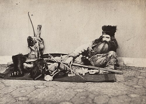 صورة فوتوغرافية تعود لعام 1864 تُظهر سيث كينمان، وهو من سكان كاليفورنيا، يعرض فروة رأس هندية (في الأمام إلى اليسار). كان يجمع "التحف الهندية" بما في ذلك فروات الرؤوس.
