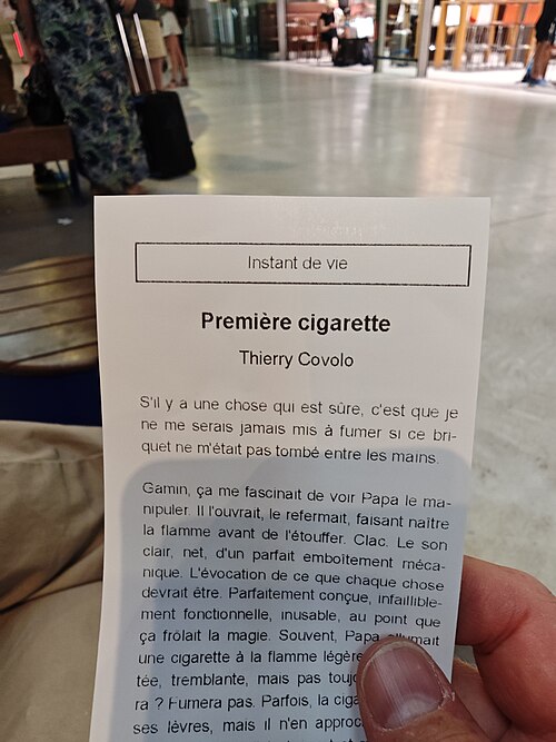 شخص يحمل كتيبًا صغيرًا مطبوعًا باللغة الفرنسية لقصة قصيرة بعنوان "Première cigarette" في مكان عام