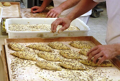 قطع صغيرة من العجين تُغطى ببذور الكتان قبل خبزها في مخبز تجاري
