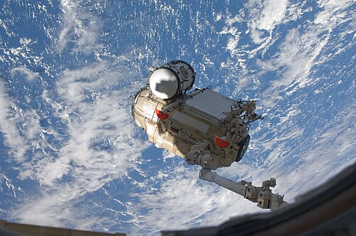 يقوم ذراع Canadarm2 بنقل MRM-1 إلى المنفذ المواجه للأرض في وحدة Zarya.