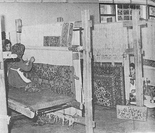 نسيج تبريز في مدرسة لصناعة السجاد في إيران عام 1975. يجلس نساج واحد على الأرض، واثنان على مقعد.