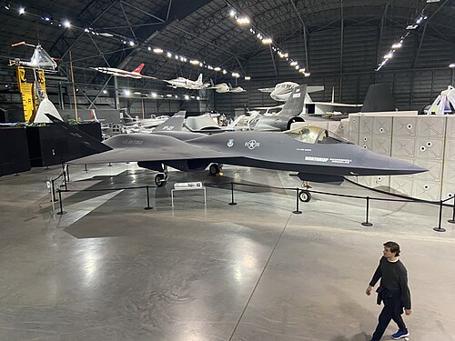 تظهر طائرة YF-23 المطلية باللون الرمادي الفحمي، والمعروفة باسم "الشبح الرمادي"، في مقدمة الصورة ووسطها، بينما يسير رجل أمامها في أسفل يمين الصورة. ويمكن رؤية العديد من الطائرات الأخرى الموجودة في المتحف خلفها.
