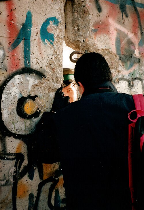 An East German guard (with cap) talks to a Westerner through a broken seam in the Wall in late November 1989.