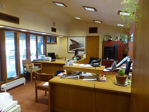 One of the building's offices. There is a desk in the foreground and windows to the left. The ceiling slopes down slightly from left to right.