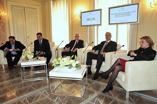أربعة رجال وامرأة يجلسون على كراسي بذراعين بيضاء مزودة بميكروفونات