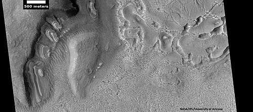 تظهر الطبقات المائلة، كما رصدتها كاميرا HiRISE ضمن برنامج HiWish، بالإضافة إلى مادة السهول العليا المضلعة الظاهرة في أعلى يمين الصورة. تتشكل هذه المادة من وحدة السهول العليا، وتتآكل بدورها لتتحول إلى منطقة الدماغ.