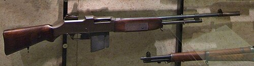 بندقية براوننج الأوتوماتيكية من طراز M1918 ذات الطراز المبكر معروضة من الجانب، مع ماسورة طويلة، وحامل ثنائي ثابت، ومخزون خشبي.