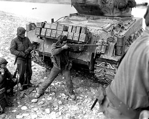 صورة بالأبيض والأسود لجندي أمريكي يصوب بندقية براوننج الأوتوماتيكية M1918A2 من خلف دبابة شيرمان M4A3(76)W HVSS، الحرب الكورية، 1951.