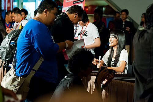 إحدى عضوات فرقة JKT48 تبتسم لأحد المعجبين أثناء توقيع كتاب