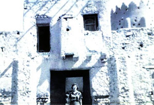 امرأة تقف أمام حصن تركي يعود إلى العصر العثماني، القطيف، 1950